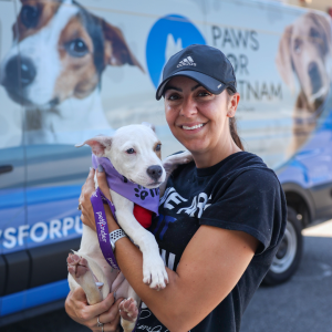 Volunteer smiling holding dog in front of Paws for Putnam van