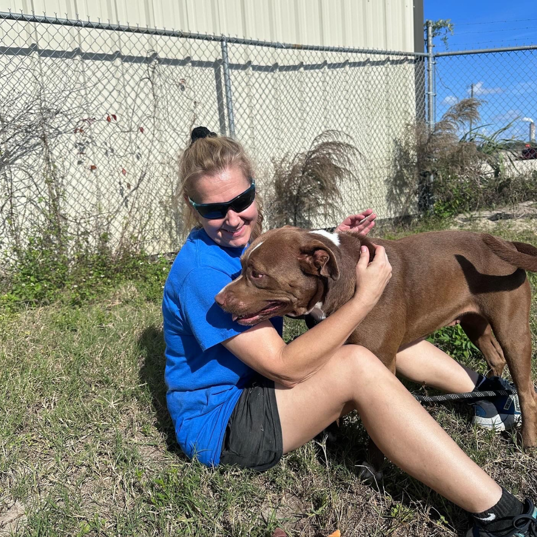 volunteer siting on ground smiling with dog in her lap